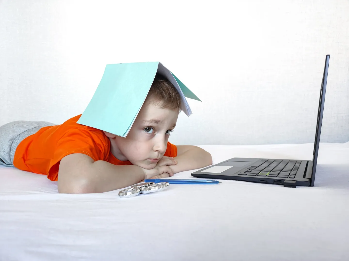 A young boy laying on the bed with his head over a laptop.